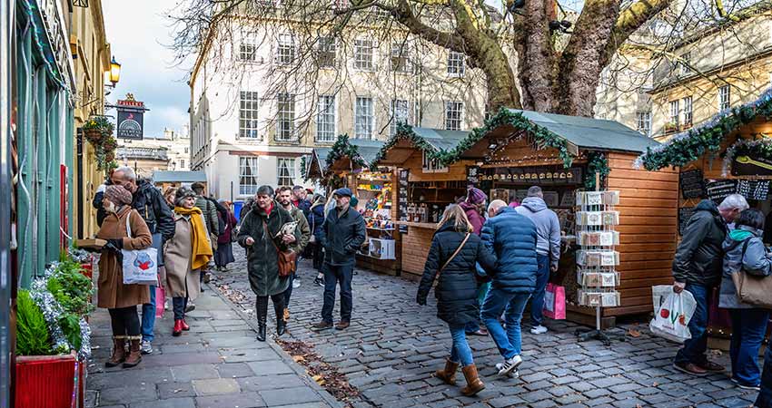 Festive Christmas market in Bath, England with people browsing wooden stalls
