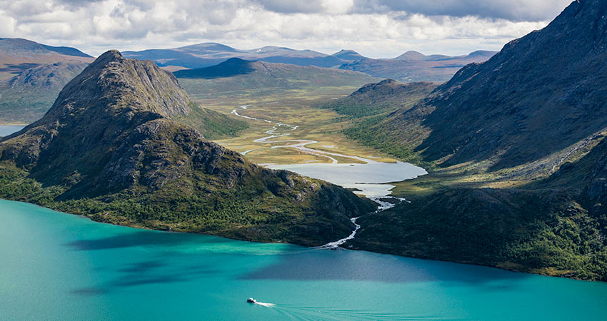 Aerial view of Besseggen Ridge in Norway with a boat crossing a turquoise lake and winding river in the distance.