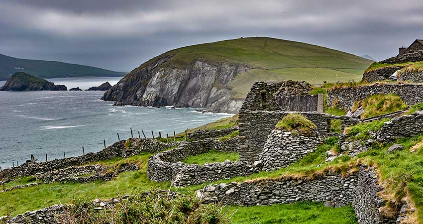Ancient stone ruins overlooking the ocean on the Dingle Peninsula, Ireland, with dramatic cliffs and rolling green hills in the background.