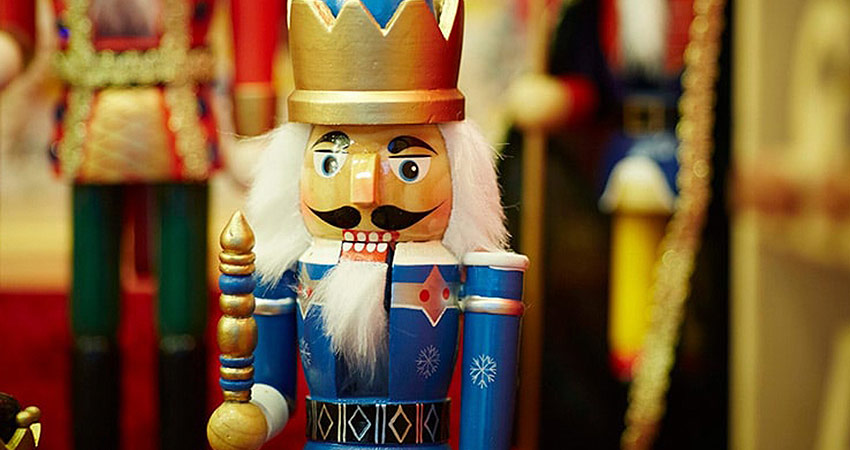Close-up of a traditional wooden nutcracker soldier in festive blue and gold, surrounded by other holiday decorations.