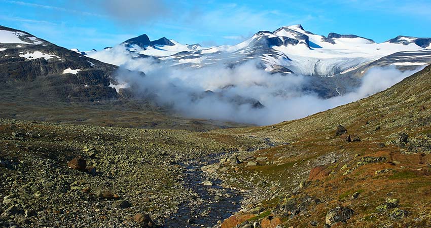 Rocky valley with clouds and Galdhøpiggen glacier peaks in Norway