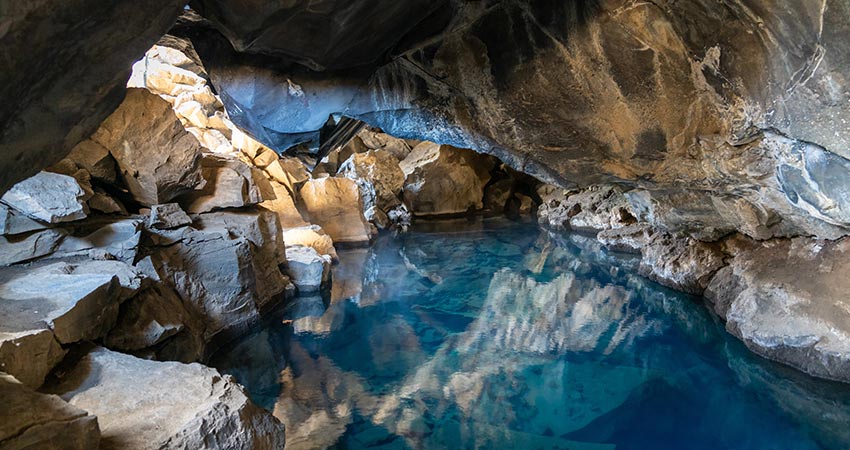 Grjótagjá cave in Iceland with crystal-clear blue geothermal water inside a rocky lava cave.