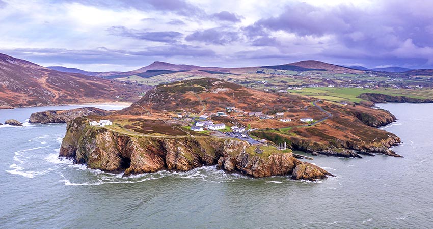 Aerial view of the Inishowen Peninsula in Ireland, showing rugged cliffs, scattered cottages, and surrounding calm seas with rolling hills in the background.