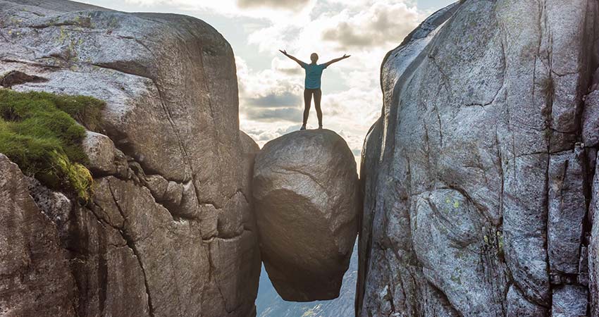 Person standing on Kjeragbolten boulder suspended between cliffs in Norway