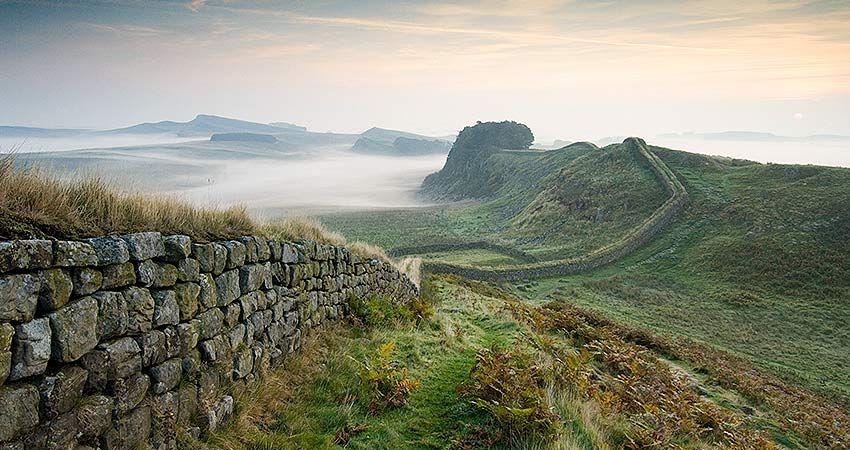 Misty morning view of Hadrian’s Wall winding through the hills of Northumberland, England.
