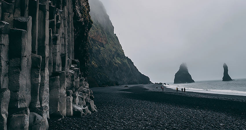 Reynisfjara black sand beach in Iceland, with basalt columns on the left and sea stacks rising from misty waters.