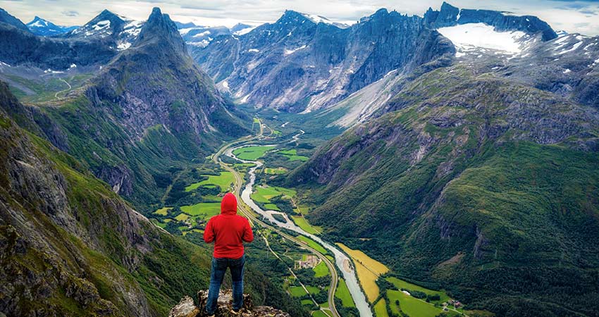 Hiker in red jacket overlooking Romsdalseggen Ridge and valley in Norway
