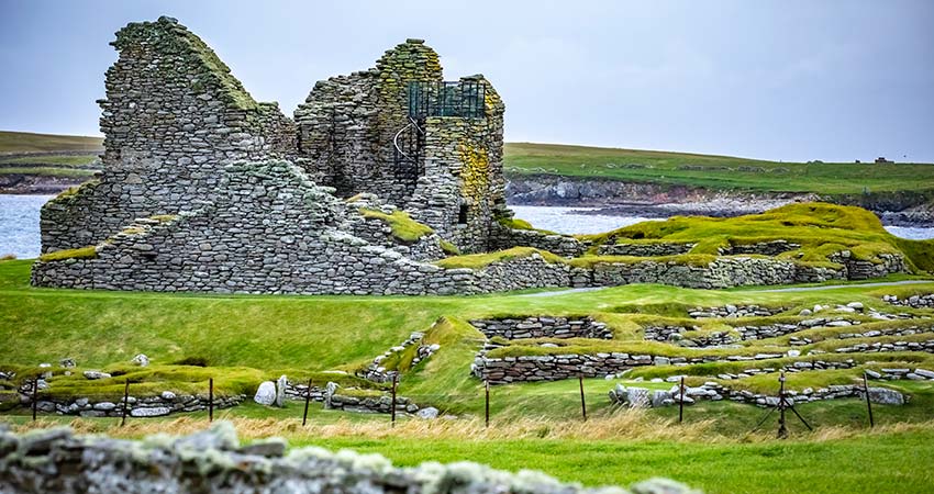 Stone ruins of an ancient castle and surrounding settlement on the grassy coast of the Shetland Isles, Scotland.