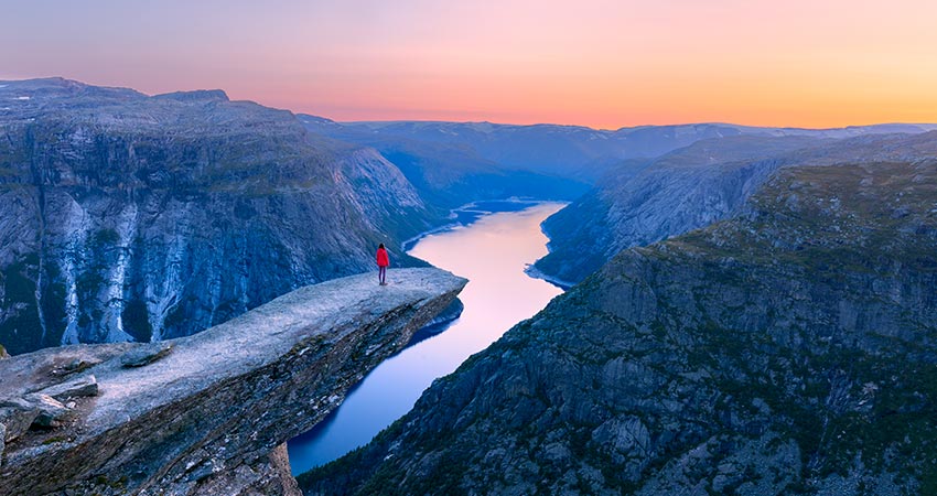 Person standing on Trolltunga cliff overlooking fjord at sunset in Norway