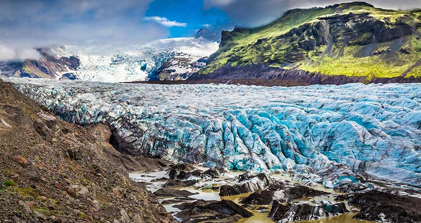 Vatnajökull glacier in Iceland, with vivid blue ice, rugged terrain, and green moss-covered cliffs in the background.