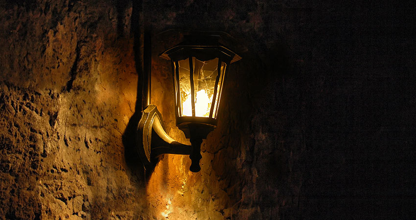 Dimly lit antique wall lantern glowing against an old stone wall with visible cobwebs.