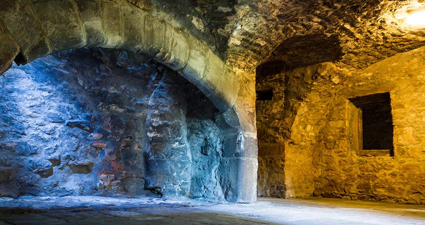 Stone vaults beneath Edinburgh Castle lit with moody blue and golden tones.