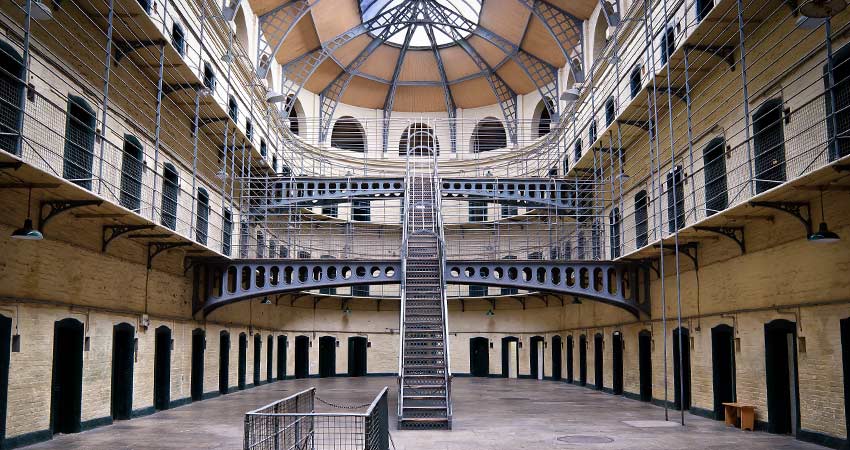 Main rotunda of Kilmainham Gaol in Dublin, Ireland, with metal staircases, walkways, and cell doors under a domed glass ceiling.