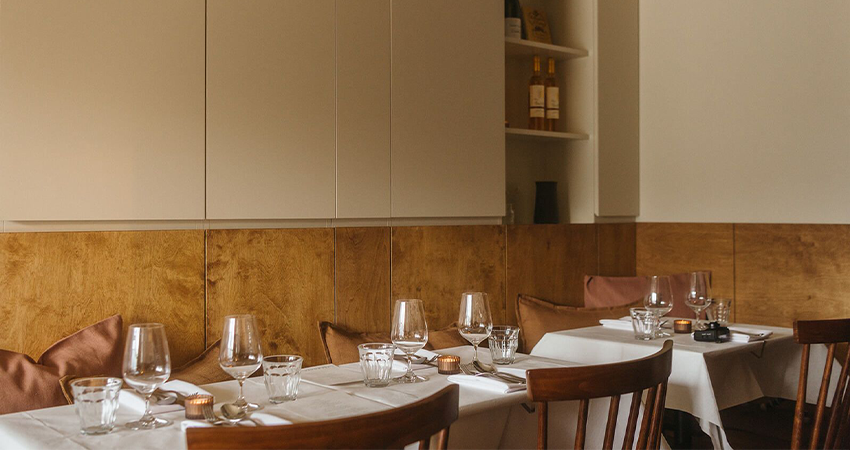 Tables set with white linens, wine glasses and candles in a wood-paneled Edinburgh dining room