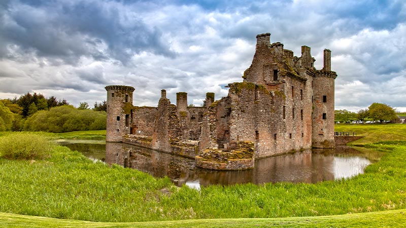 Ruins of Caerlaverock castle surrounded by mall body of water and lush landscape