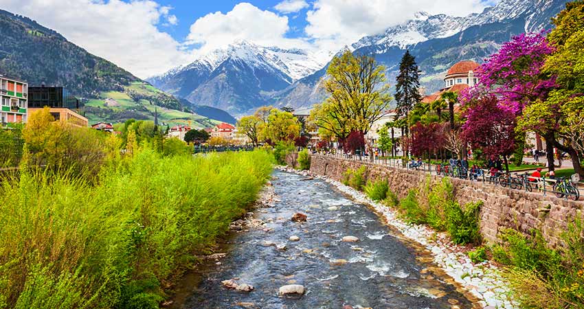 Quaint town of Merano, Italy, showing river flowing through it and a snow covered Dolomite mountain range in the background