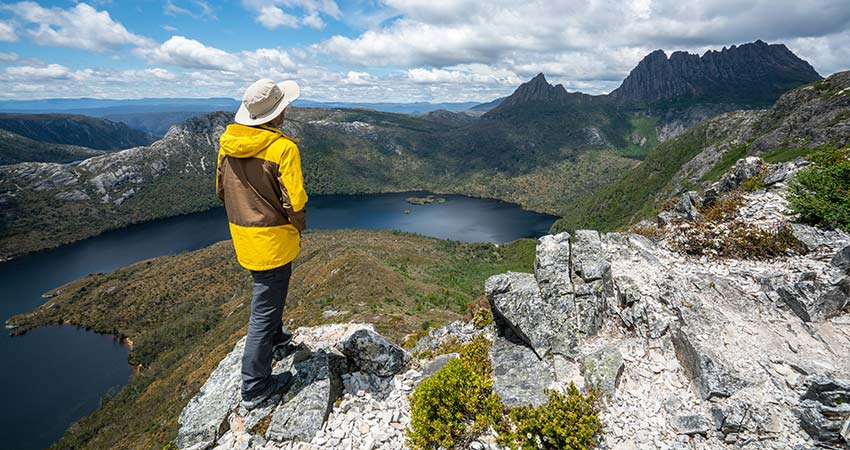 Traveler on top of mountain looking at distant Cradle Mountain in the Tasmanian Wilderness 