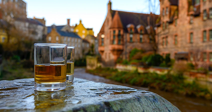 Two whisky glasses with buildings old town Scotland in the foreground